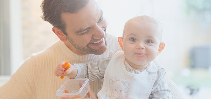 Padre sosteniendo a su bebé mientras come zanahoria